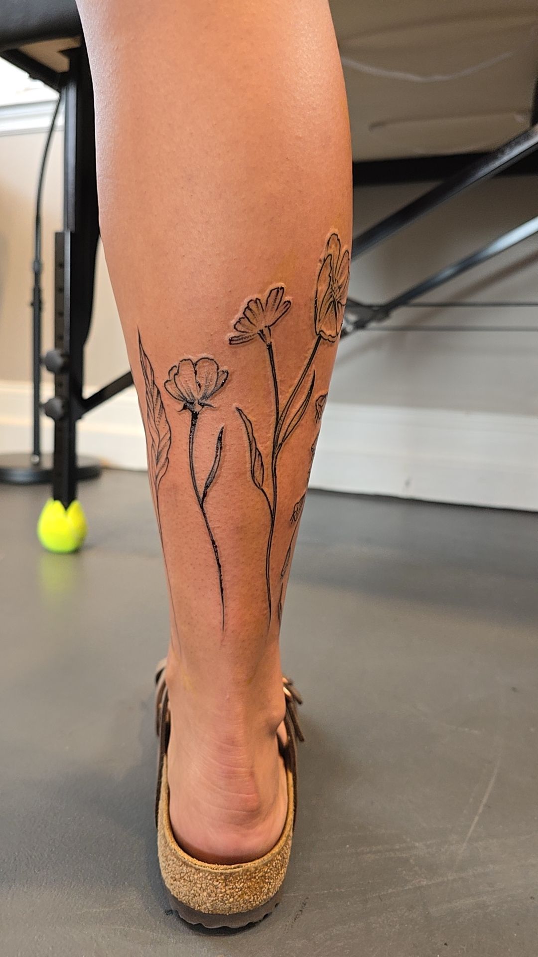 Rear view of a fine-line wildflower leg tattoo by Billy Smith
