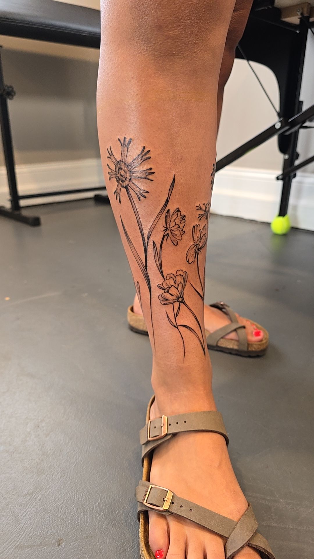 Fine-line flowers flowing along the front of a lower leg by Billy Smith